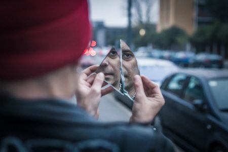man standing on city street holding broken mirror