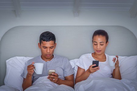 man and woman relaxing in bed looking at their cell phones