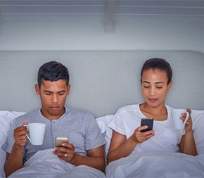 man and woman relaxing in bed looking at their cell phones
