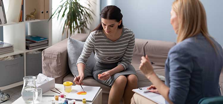 woman therapist holds clipboard and asks patient to paint