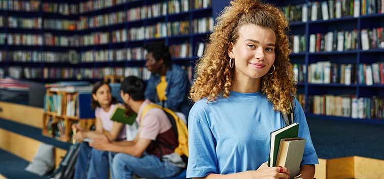 woman holding books stands in college library
