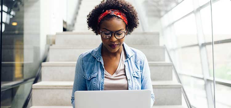 woman sits on stairs and studies on her laptop