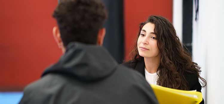 sports psychologist sits and converses with athlete in gymnasium