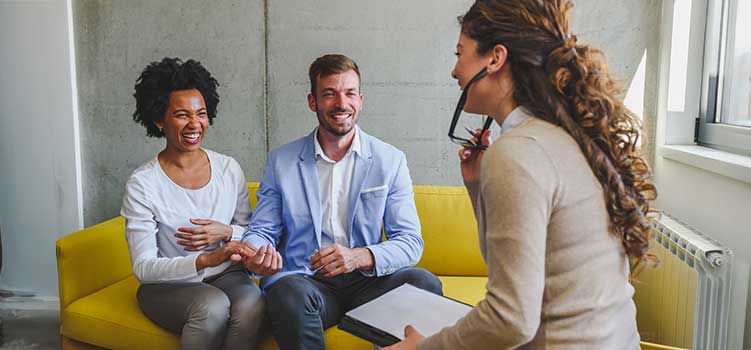 couple in marriage counseling share a lighter moment with their marriage and family therapist in california